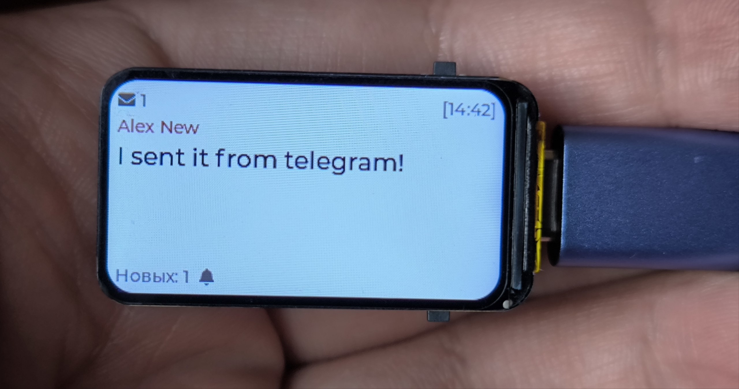 ESP32-C6 pager in a hand showing a Telegram message on its LCD